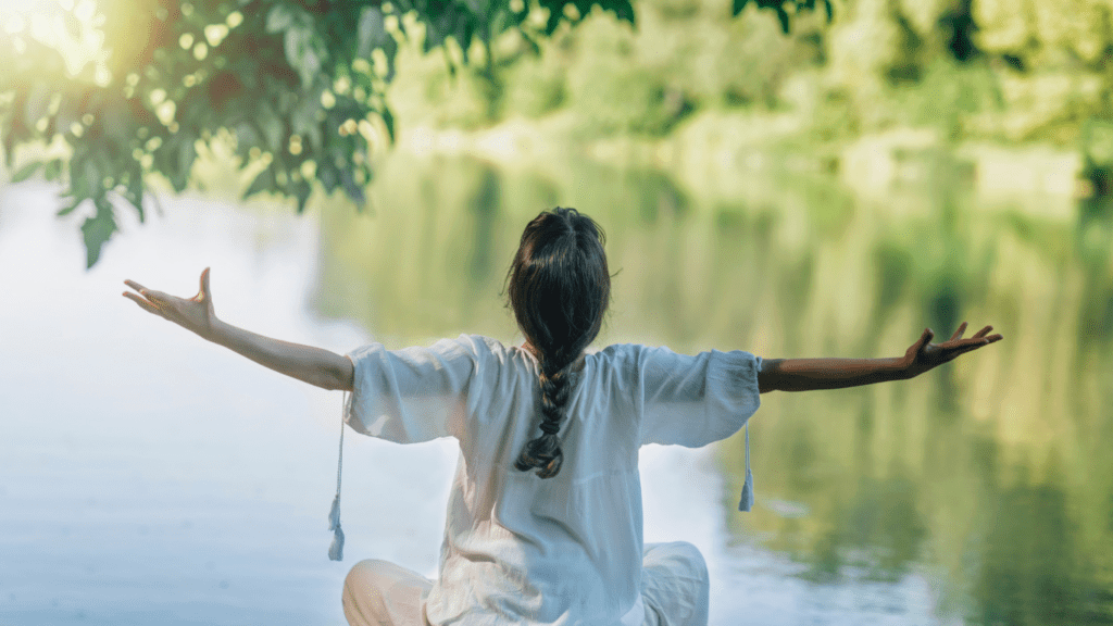 a person sitting on a log by a lake with their arms outstretched