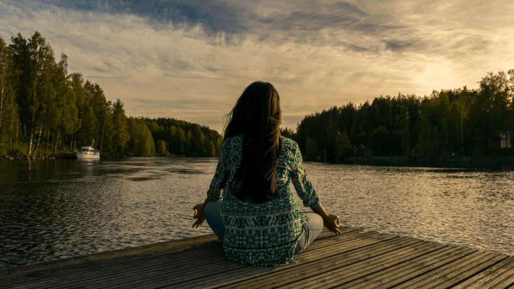 a person sitting on a log by a lake with their arms outstretched