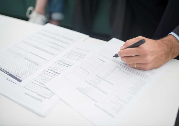 Hand with Pen on Documents on Desk